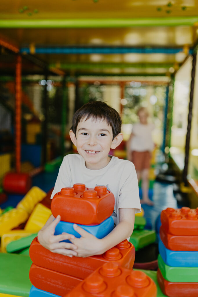 Ein lächelnder Junge stapelt große bunte Bausteine im Indoor-Spieleland des Familienhotels Gut Landegge.