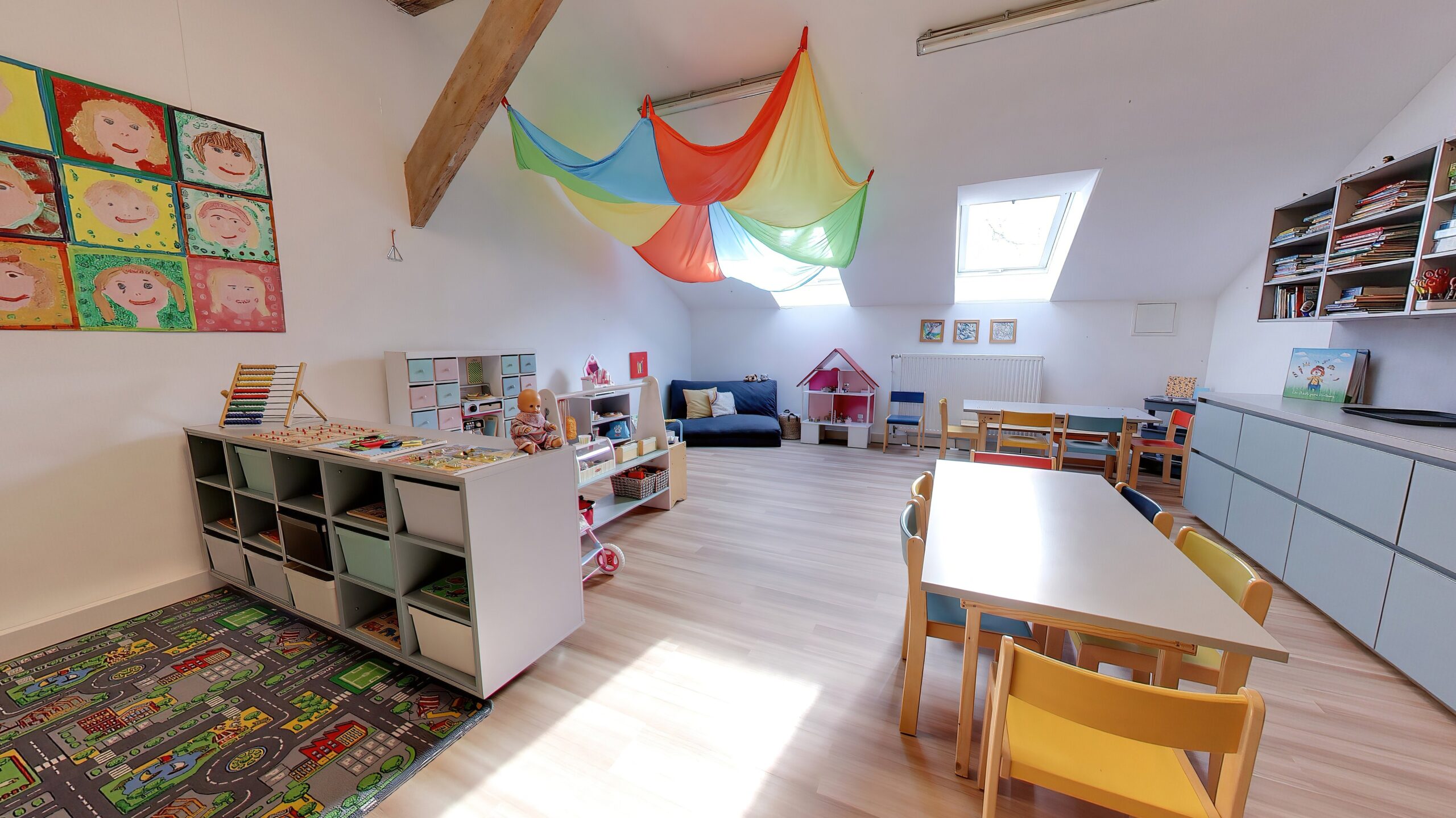 Unter der Dachschräge bietet der helle Gruppenraum Spielzeugregale, Kindertische, eine Puppenecke und bunte Tücher an der Decke.