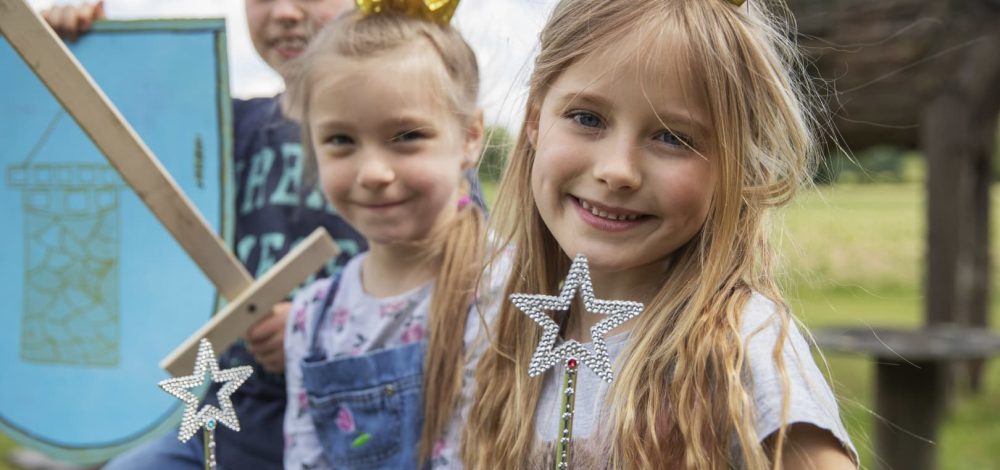 Familienhotel Gut Landegge im Emsland: zwei Mädchen mit Krone auf dem Kopf lächeln in die Kamera und ein kleiner Junge im Hintergrund
