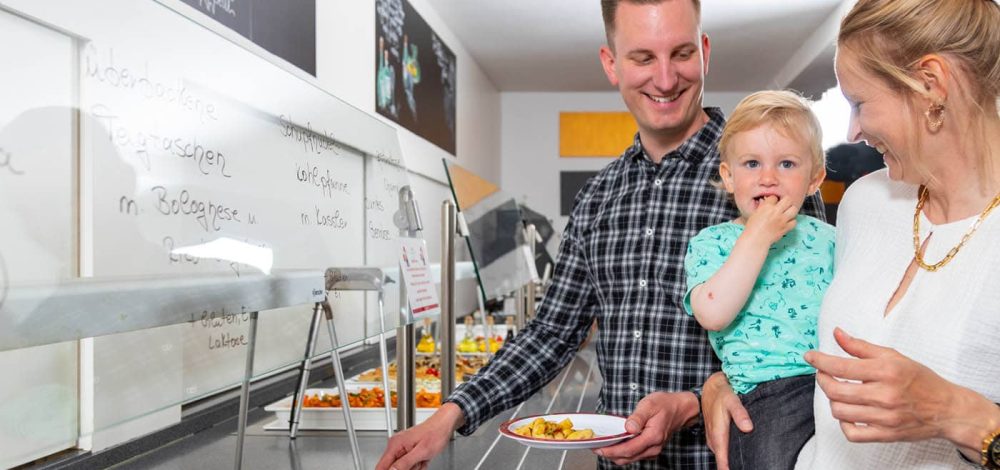 Familienhotel Gut Landegge im Emsland: Eltern mit Kind am Buffett, für das Kind gibt es lustiges kindgerechtes Geschirr.