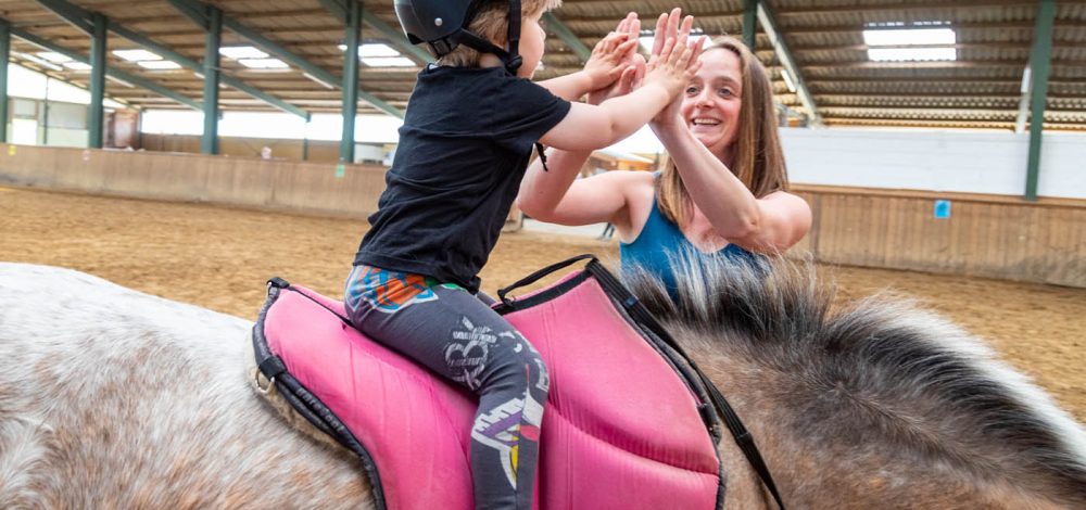 Familienhotel Gut Landegge im Emsland: Kind auf dem Pferd macht High five mit der Betreuerin