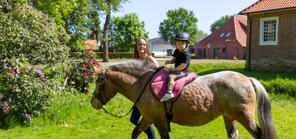 Familienhotel Gut Landegge im Emsland: Kind auf Pferd draußen in der Natur vor dem Gut